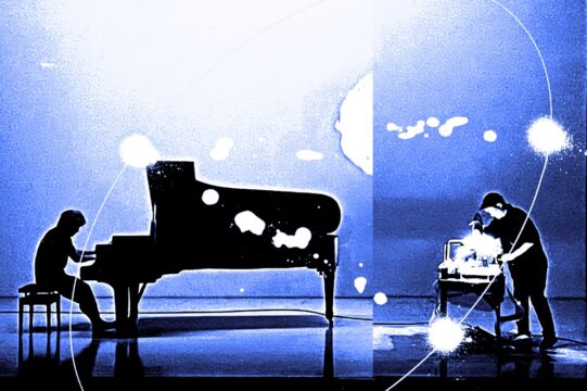 コラボレーション・パフォーマンス 鈴木まさと かける 鈴木ヒラク『Prologue』のアイキャッチ画像です。画像は、深い青と光の白をベースにして、スタイリッシュな雰囲気に加工してあります。左にグランドピアノを弾く鈴木まさとさん、右にデスク上に置かれた機材のようなものを前かがみになって触る鈴木ヒラクさんの姿が黒いシルエットとして写っています。