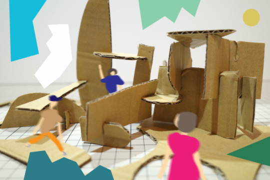 「砂浜にお城をつくろう」のアイキャッチ画像です。ダンボールで作られた小さな建物のような立体物が、方眼紙の上に組み立てられて置かれています。写真とデジタルイラストを組みわせたような画像で、周囲には、人物3人のイラストが描かれています。手前の人物は、強めのピンクのワンピース、左の人はベージュのトップスに橙色のパンツ、奥の人は紺色のトップスを着ています。背景にはカラフルでポップな図形がポイントとして入っています。
